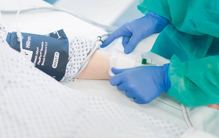 Einem Patienten wird Blut abgenommen. Die Pflegekraft trägt Schutzkittel und Schutzhandschuhe.