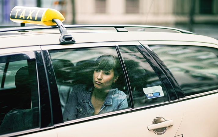 Eine Frau sitzt in einem Taxi und schaut gedankenverloren auf dem Fenster.