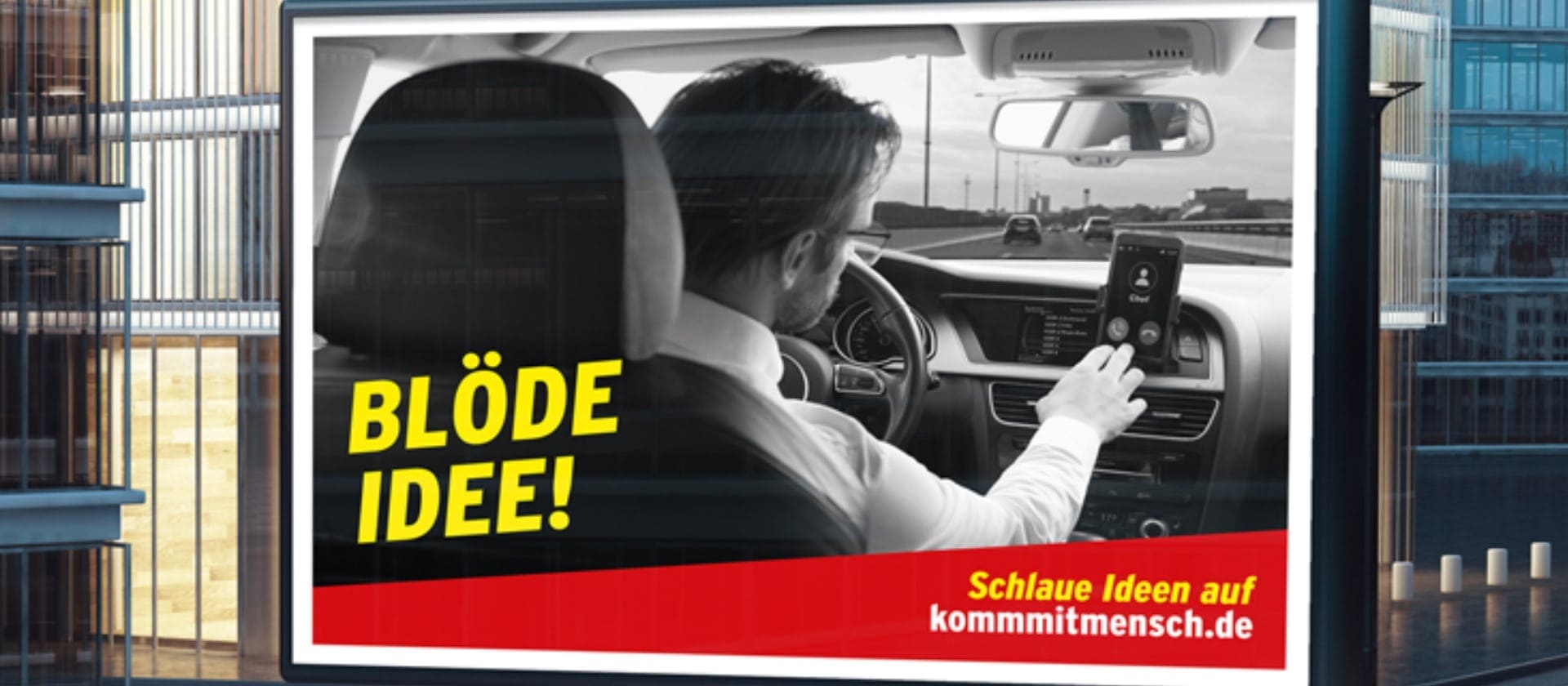 Zu sehen ist ein Werbeplakat, dass Verkehrsunfälle wegen Unaufmerksamkeit am Steuer verhindern soll. Es zeigt einen Mann, der am Steuer auf sein Handy tippt.