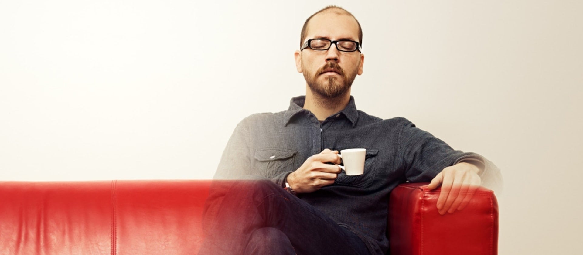 Abbildung eines Mannes, der mit geschlossenen Augen auf einer roten Couch sitzt und einen Espresso trinkt.
