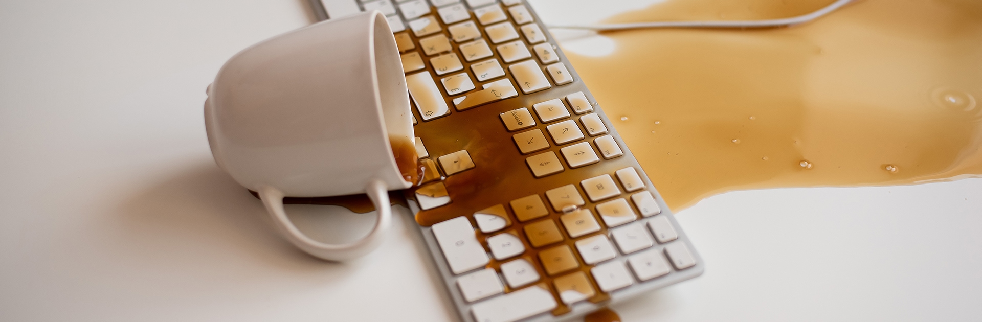 Kaffee läuft aus einer umgekippten Tasse über eine Tastatur