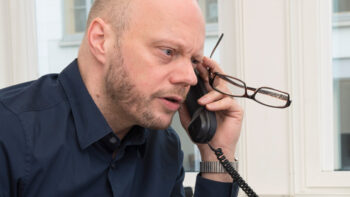 Ein Mann sitzt am Schreibtisch und telefoniert mit gestresstem Blick.